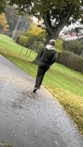 A Man In A Black Jacket Is Running Down A Path