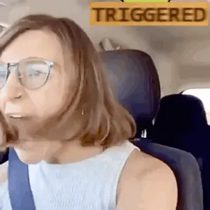 A Woman Wearing Glasses Is Sitting In A Car With A Yellow Sign That Says Triggered