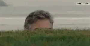 A Man Peeking Out From Behind A Grassy Hill