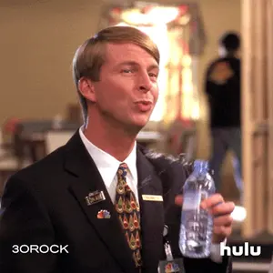 A Man In A Suit And Tie Is Holding A Bottle Of Water With The Hulu Logo In The Background