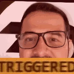 A Man With Glasses And A Mustache Is Holding A Sign That Says Triggered .