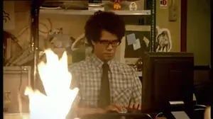 A Man In A Plaid Shirt And Tie Is Typing On A Computer With Flames Coming Out Of The Screen