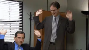 Two Men In Suits And Ties Are Waving Their Hands In A Room